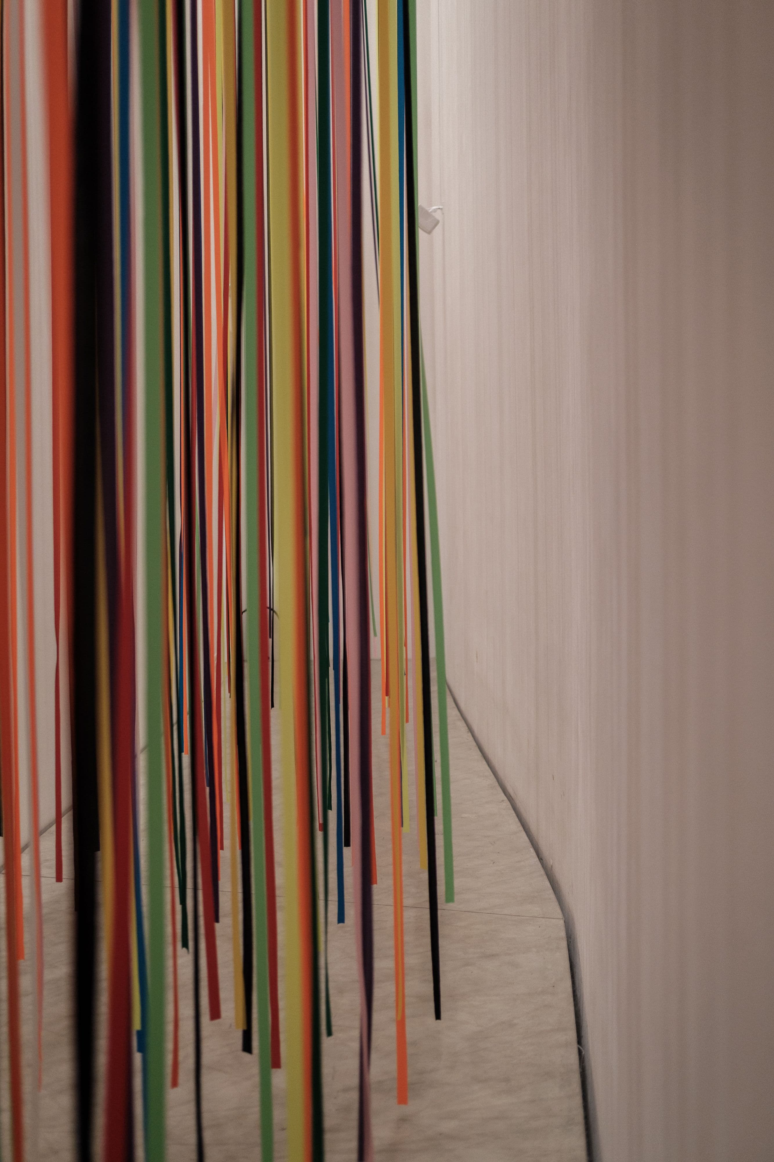 A close-up view of vibrant, colorful strips hanging vertically in a minimalist gallery space.